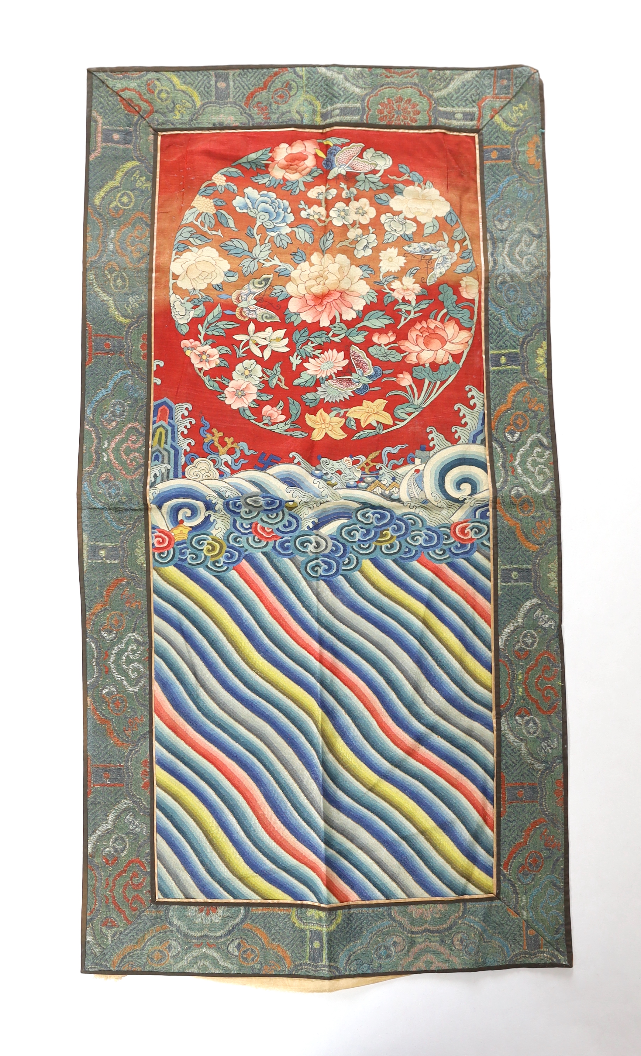 A Chinese Kesi polychrome silk woven panel, Qing dynasty, first half 19th century, possibly the back of a robe, decorated with a roundel of flowers and butterflies above a border of ‘lishui waves’ and auspicious good for